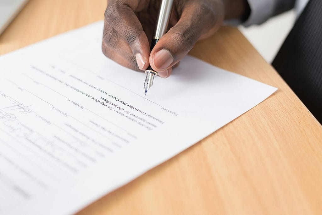 Mãos assinando documento de inventário — decisão entre valor histórico e valor de mercado na herança para o Imposto de Renda